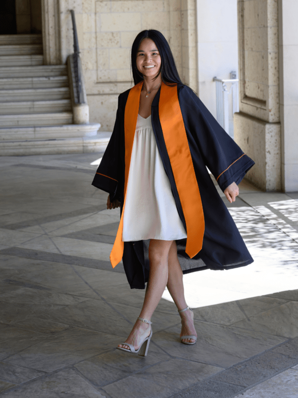 A young woman smiling confidently, dressed in a graduation gown and cap, adorned with a vibrant graduation stole, ready for her graduation ceremony.