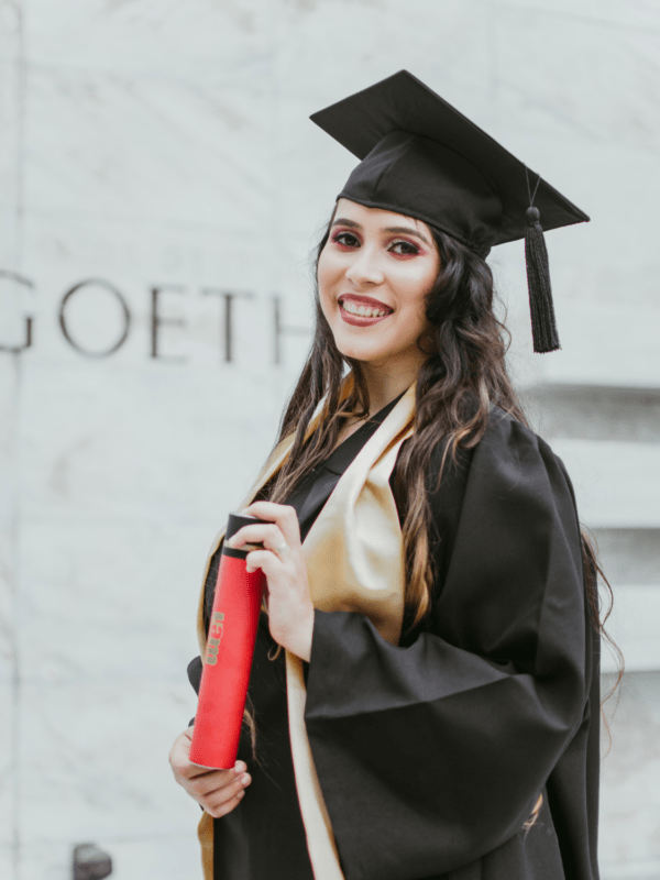A young woman smiling with confidence, dressed in a graduation cap and gown, with a vibrant stole draped over her shoulders, ready to celebrate her academic achievements.