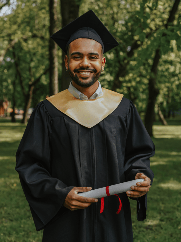 A young man beaming with pride, dressed in a graduation cap and gown, with a distinguished stole draped over his shoulders, ready to celebrate his academic success.