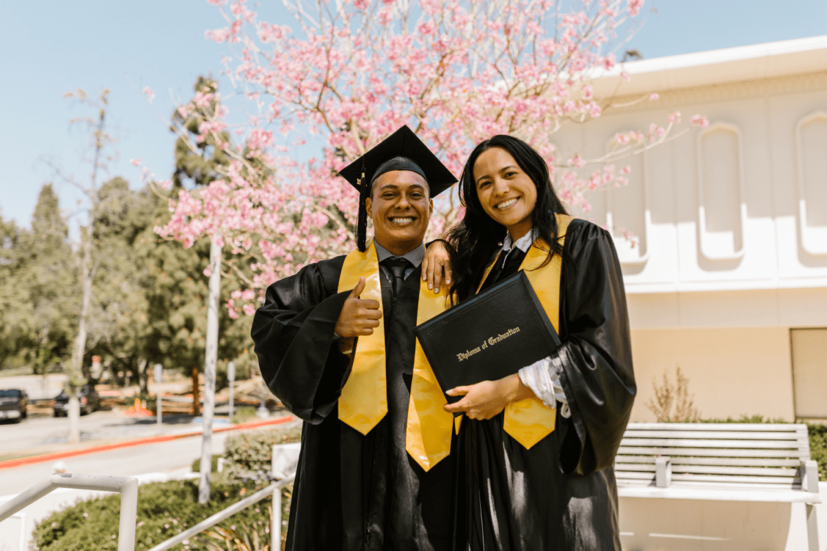 Two friends, dressed in graduation caps and gowns, standing side by side with beaming smiles, celebrating their academic achievements and friendship.